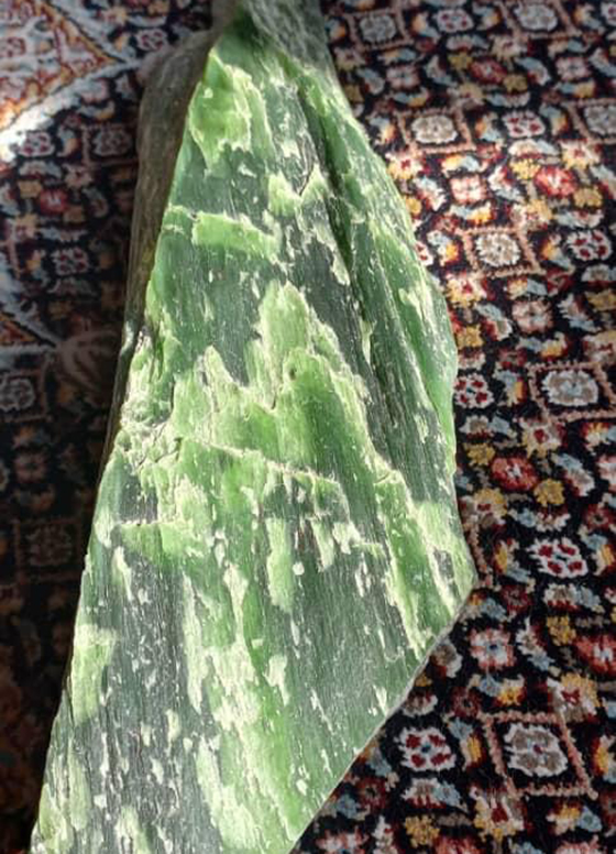 A large shard of green nephrite lies on an ornamental carpet.
