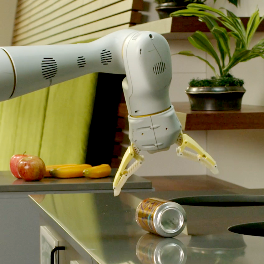A robot with one arm attempts to pick up a drinks can from a kitchen surface