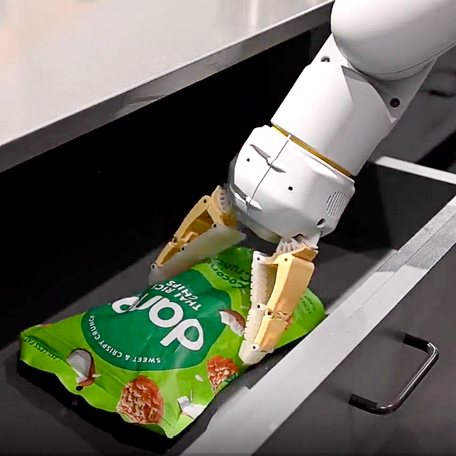 A robot arm with grippers attempts to pick up a packet of crisps
