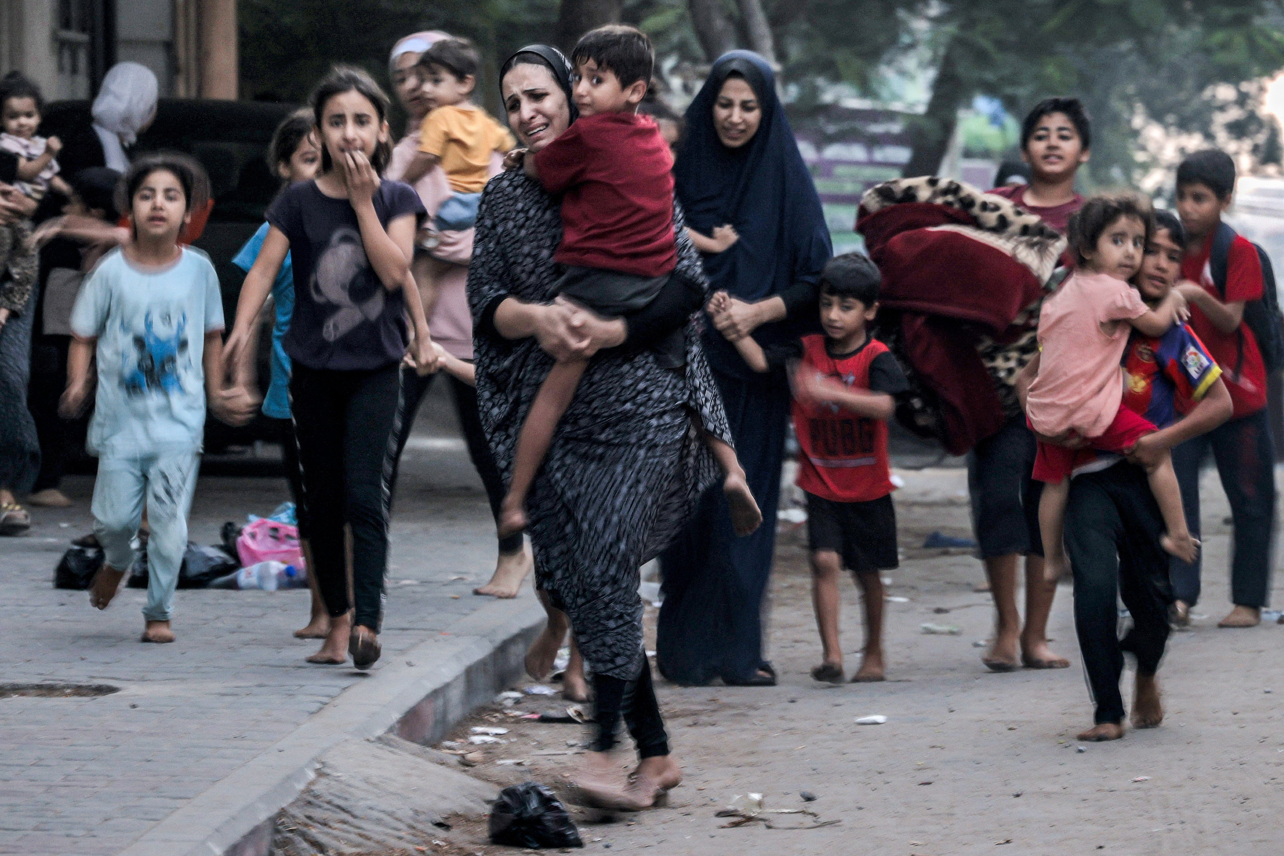 A group of women and children with distressed faces hurry along an urban-looking street