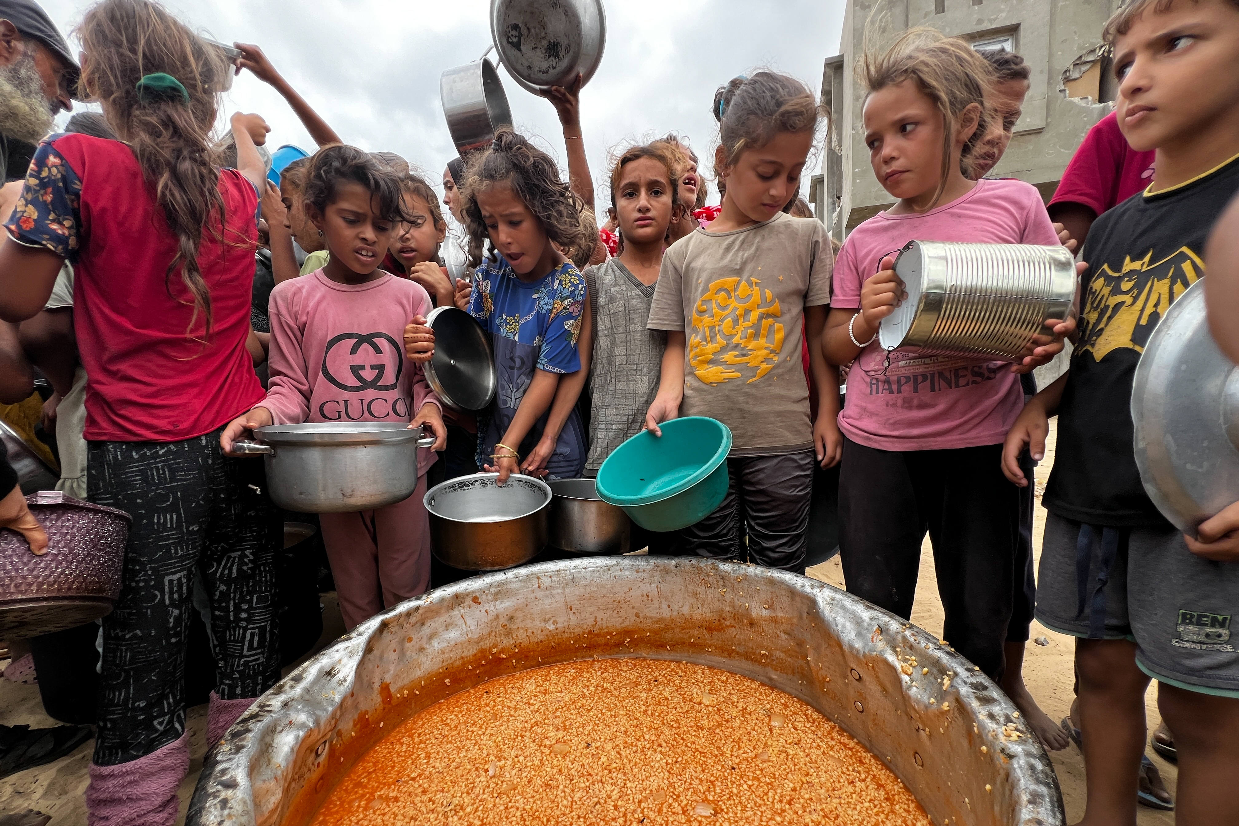 A crowd of children holding metal bowls wait for food to be distributed