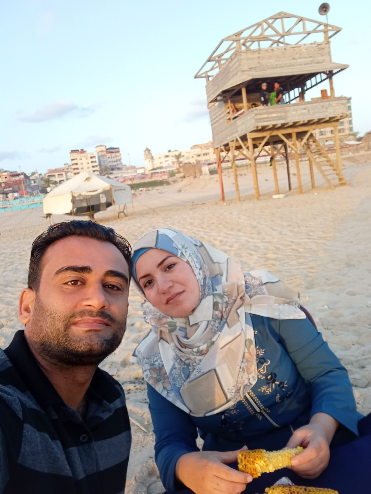 Ramy and his wife Fatheya sitting together on a beach while eating corn on the cob