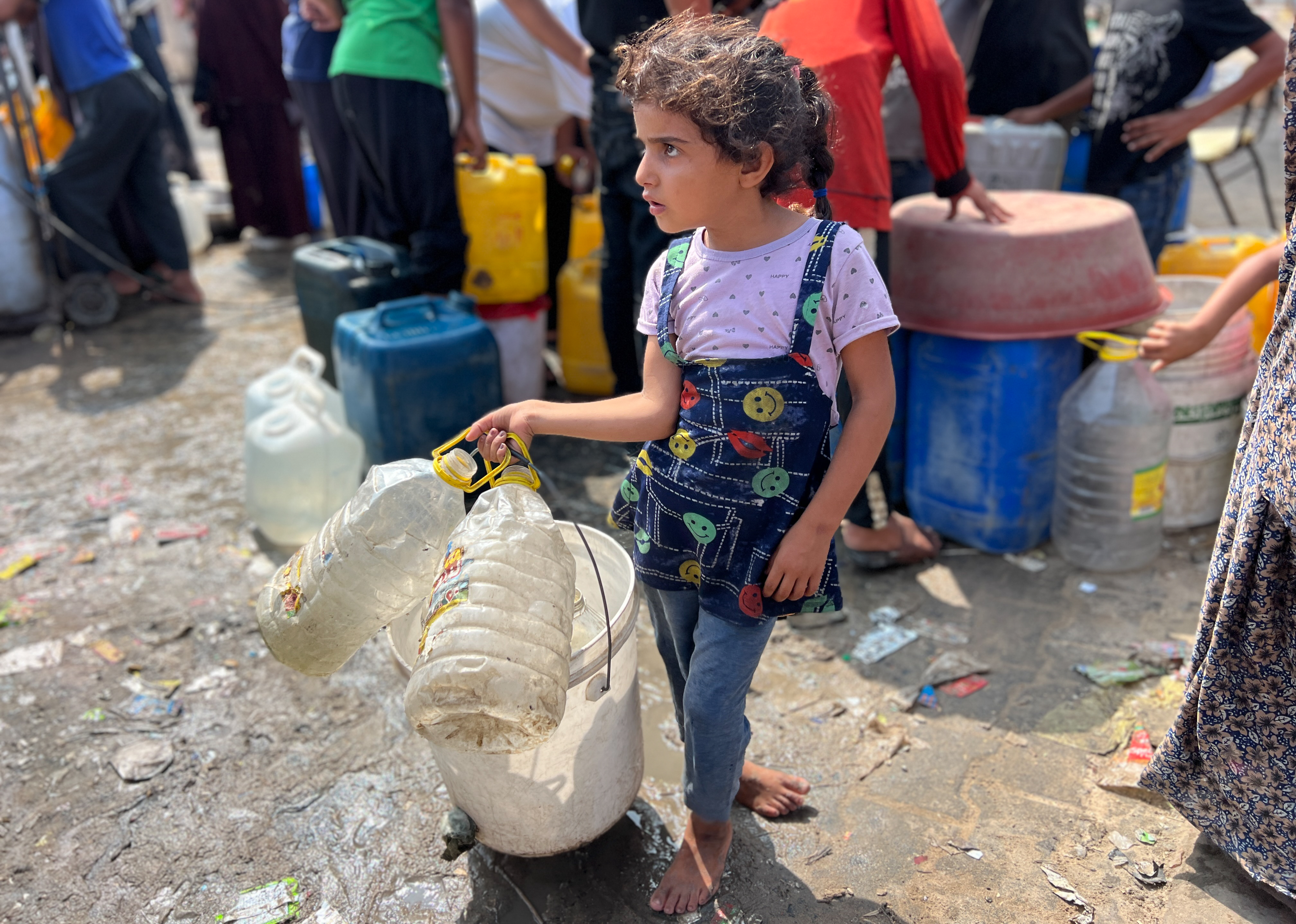 A small child holds dirty jugs for storing water