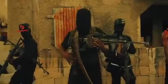 Three armed individuals wearing dark clothing and masks stand in front of a rough stone building, each holding rifles and one draped with an ammunition belt.