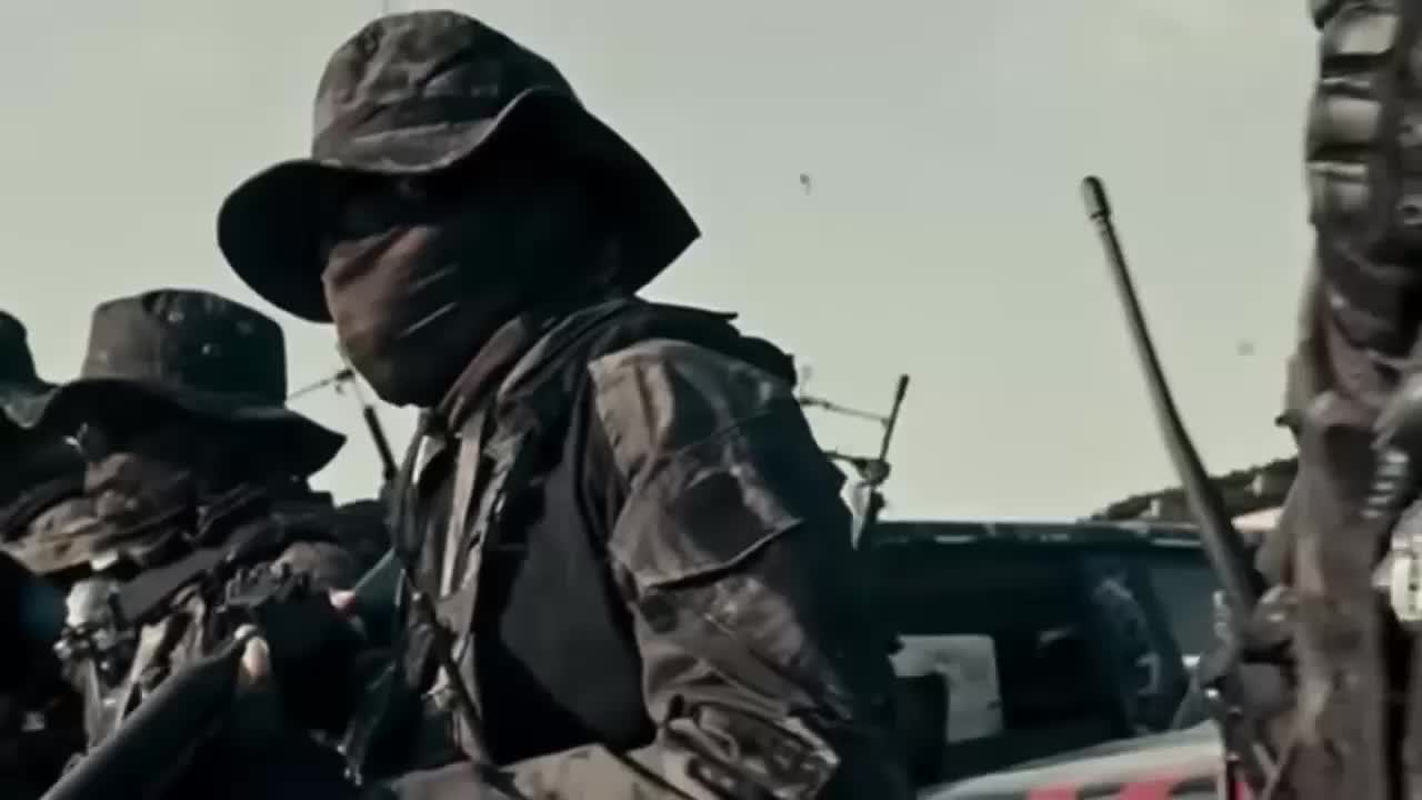 A group of soldiers in camouflage attire and face coverings stand alert with weapons, against an outdoor backdrop.