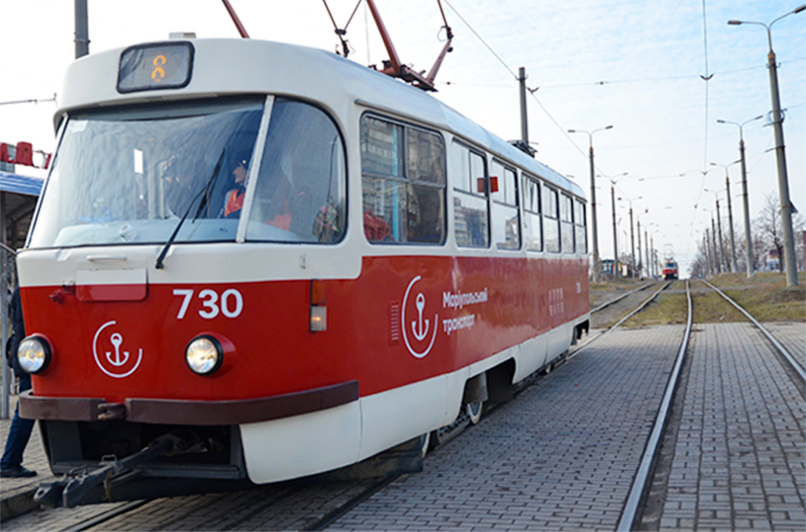 A white-and-red streetcar sits at a stop as passengers board.