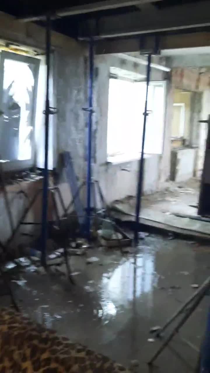 An apartment in half-built condition. Temporary props are holding up ceiling, as water runs down the walls to pool on the floor.