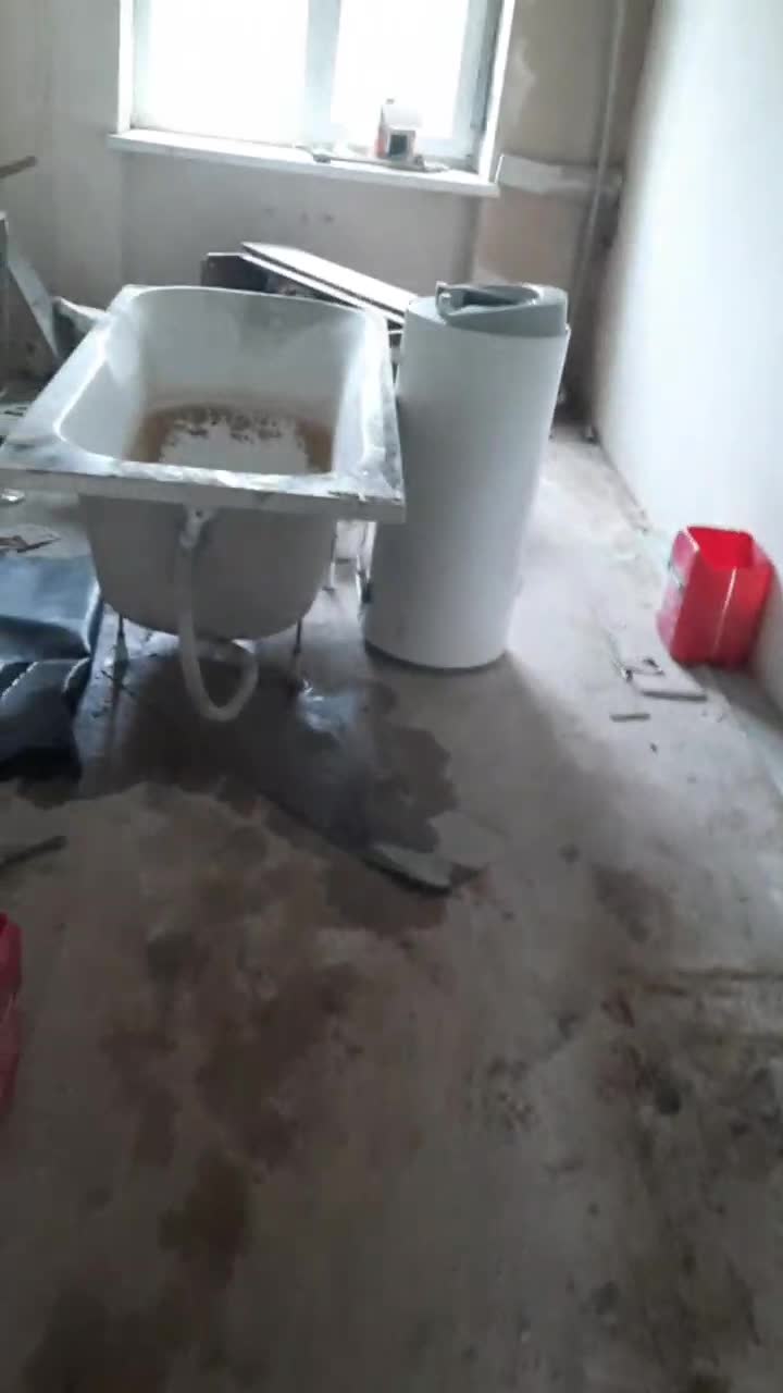 An unfinished bathroom with damp stains on wall, mould on the ceiling, and exposed plumbing and wiring.