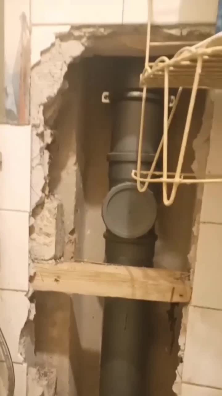 A hole has been cut into a bathroom wall, exposing the sewage pipe behind.