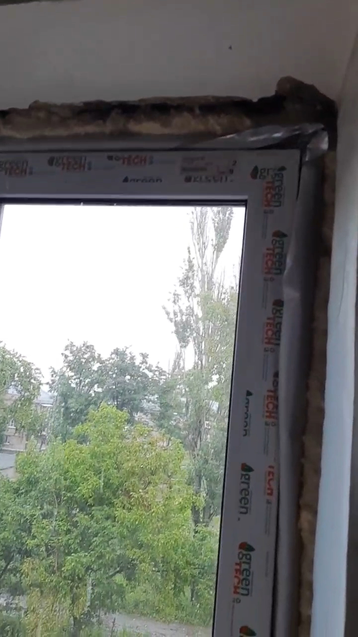 Still image from a video inside an apartment, showing poorly-fitted insulation foam surrounding a window.