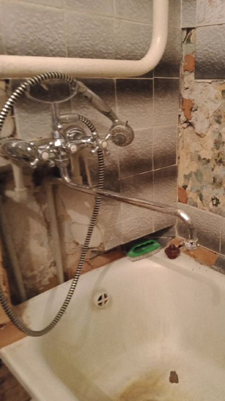 Still image from a video inside an apartment, showing a bathtub with broken tiles and mould growing on the walls.