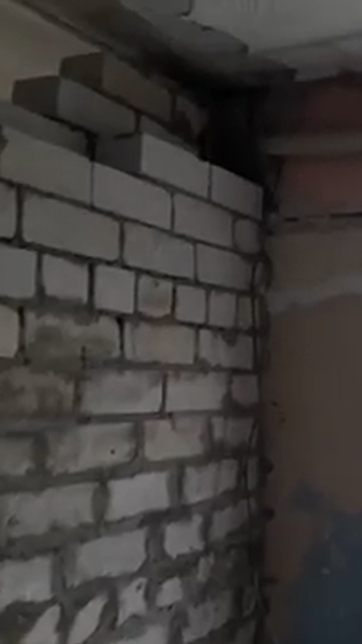 Still image from a video inside an apartment, showing an unfinished cinderblock wall with sloppy masonry.
