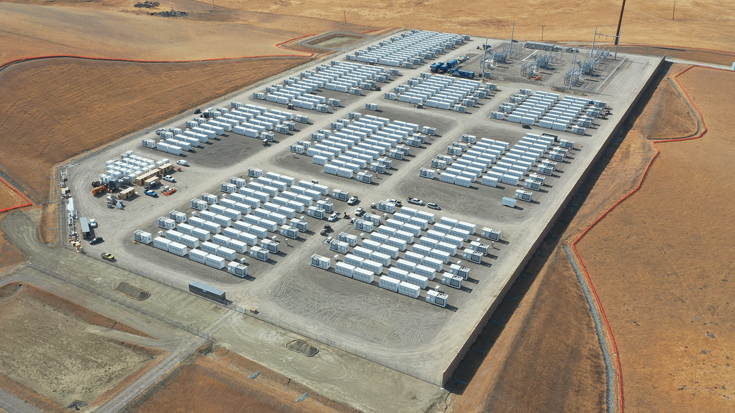 Aerial view of the Kola Energy Storage battery facility in California. Many dozen or hundred very large batteries, resembling shipping containers are visible.