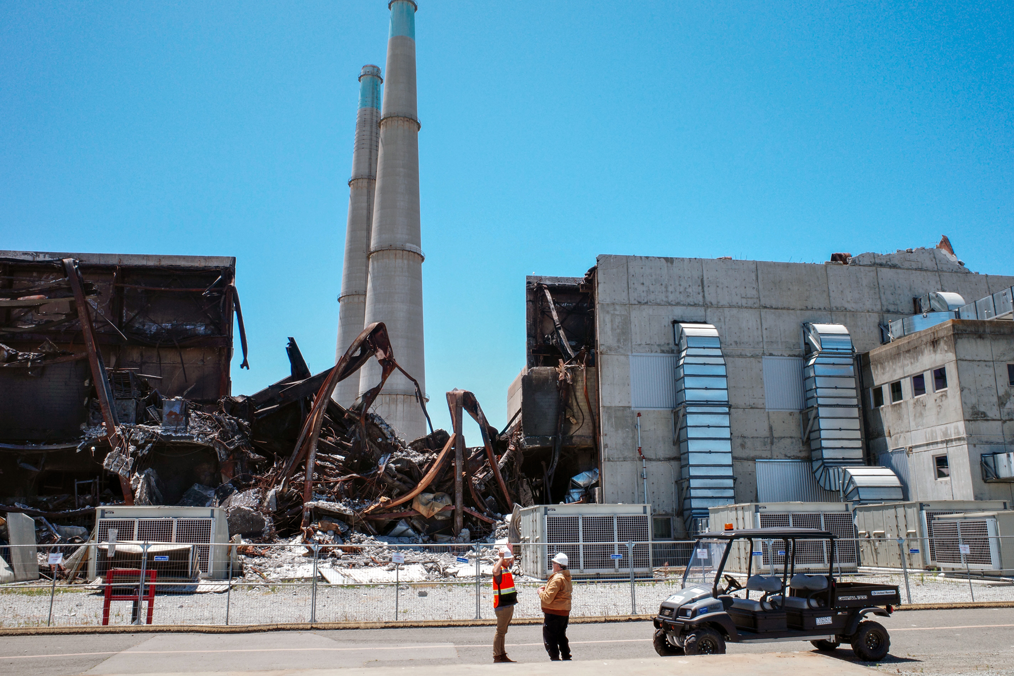 The exterior of the Moss Landing battery site damaged by a fire. Construction workers can be seen in the foreground.