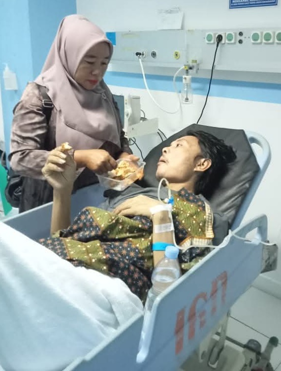 Alt text for image 4: Bunanda lies in a hospital bed looking thin with an IV drip attached to his arm, as his wife Erna feeds him.