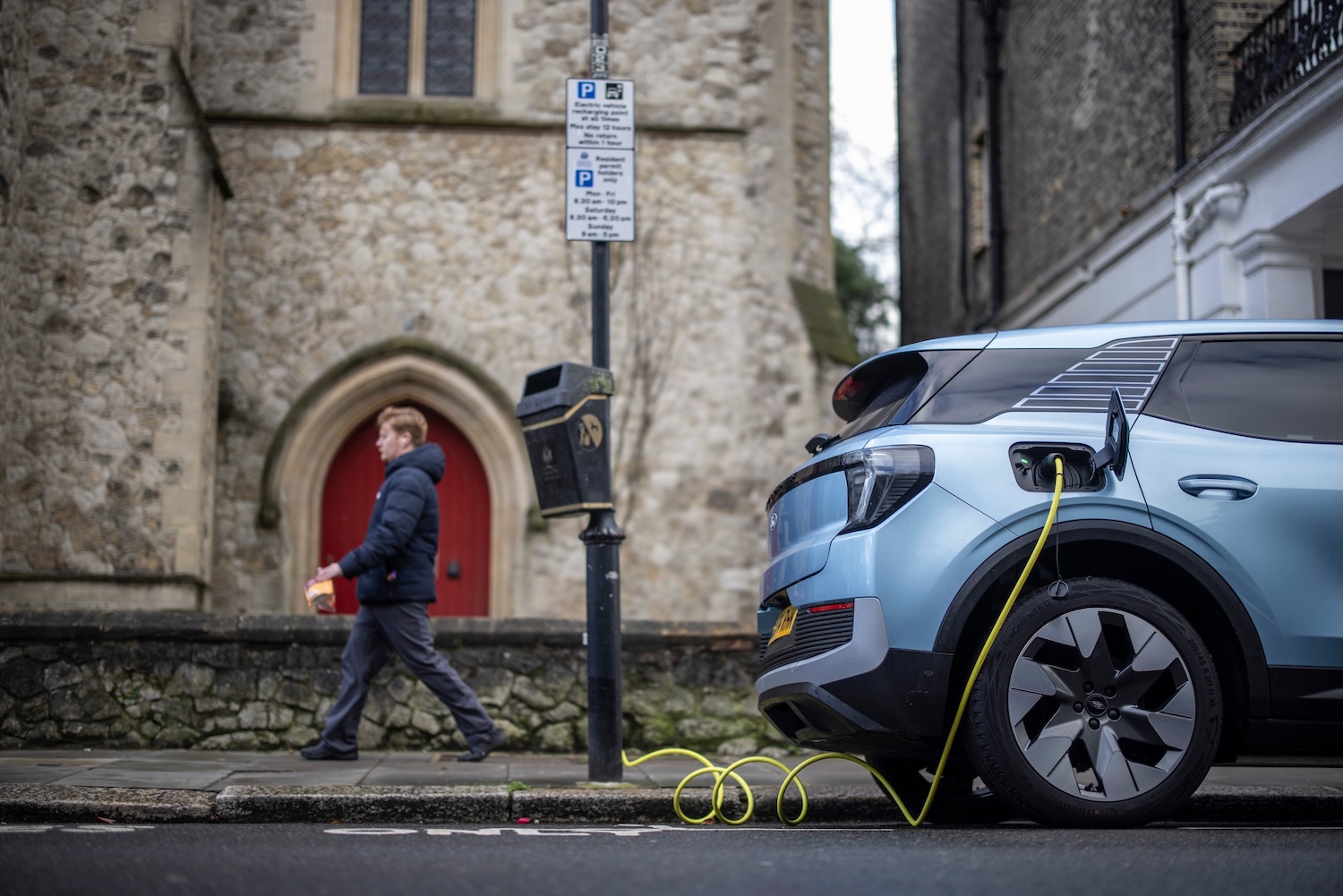A light blue electric vehicle uses a lamp-post plug-in point on a street in front of a church in London’s borough of Kensington and Chelsea