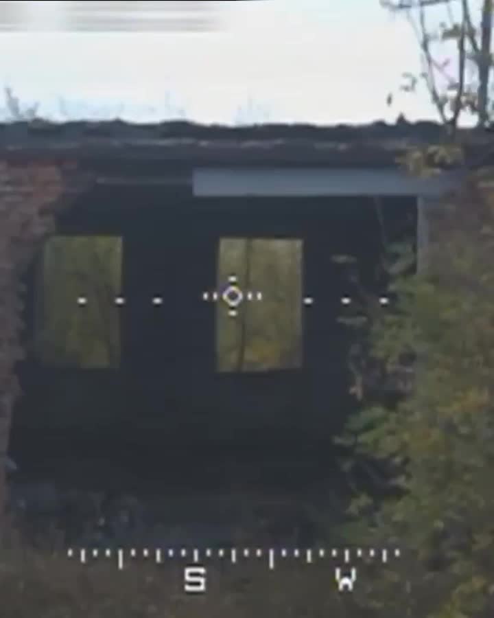 Dark, damaged building facade with two rectangular window openings, seen through a sight reticle and compass markings.
