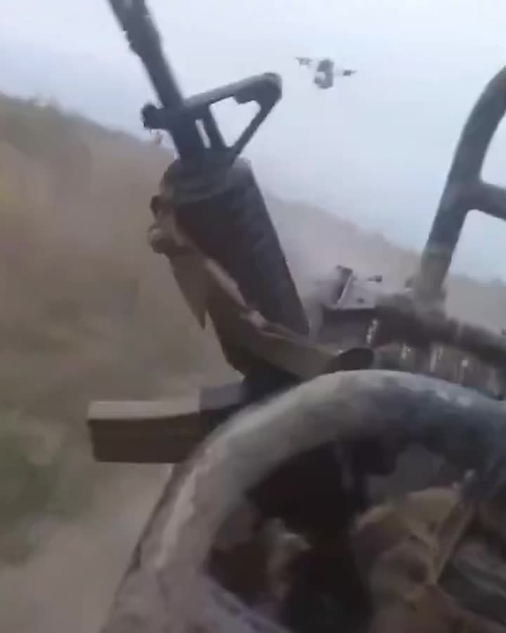 View from behind a vehicle-mounted machine gun: the rifle barrel and linked ammunition belt over a dusty hillside.