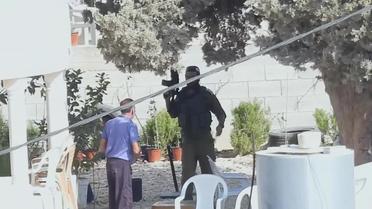 A video showing two men in military dress with rifles advancing on an unarmed man standing at the front of a white house. One of the armed men shoves the unarmed man with the barrel of his gun. The unarmed man retreats into the house and the two men walk away.